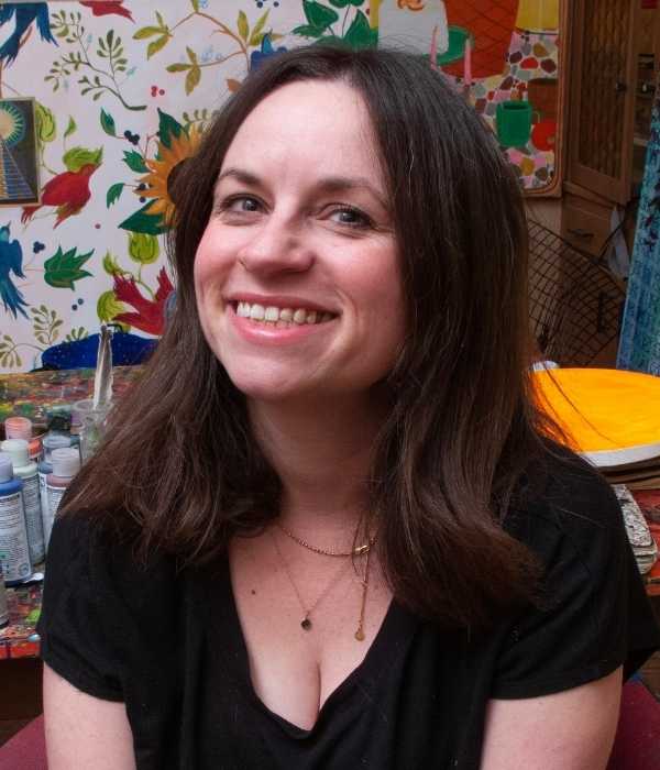 Smiling person with brown hair and light skin sitting in front of a colorful background.