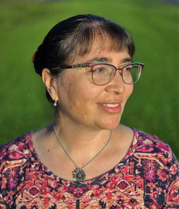 Smiling person with tied back hair and glasses in front of a green background.