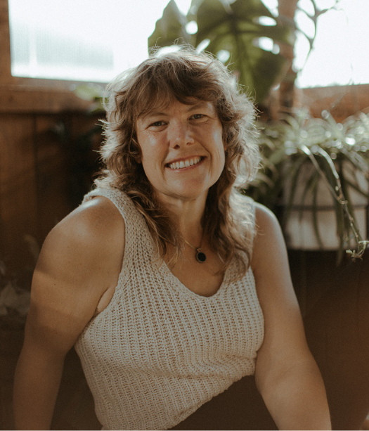 Smiling person with shoulder length brown hair, sitting on floor