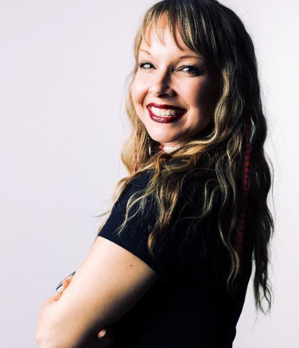 Smiling person with long hair and bangs, looking over their shoulder at the camera.